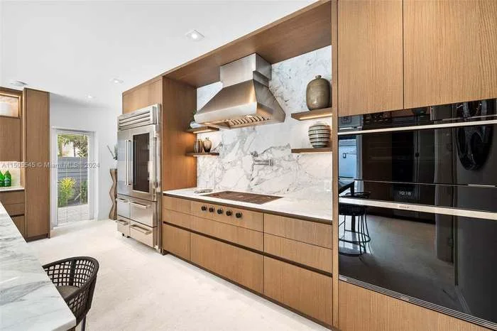 After: wood cabinetry wall with built-in ovens and a marble slab backsplash