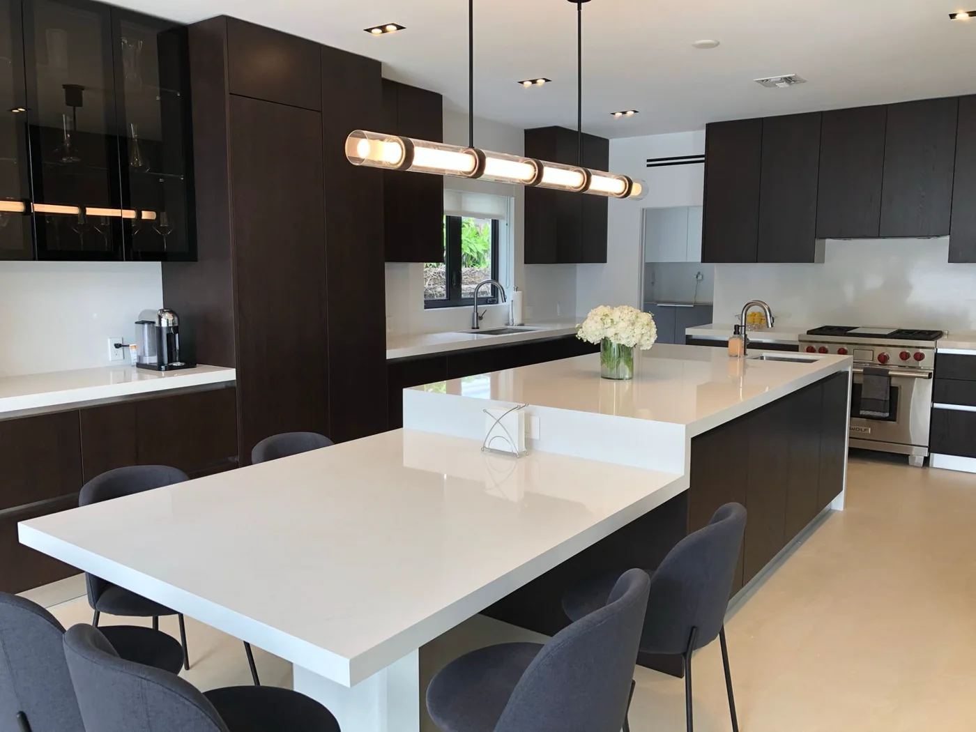 The kitchen after: dark wood cabinetry, a white waterfall island and pendant lights