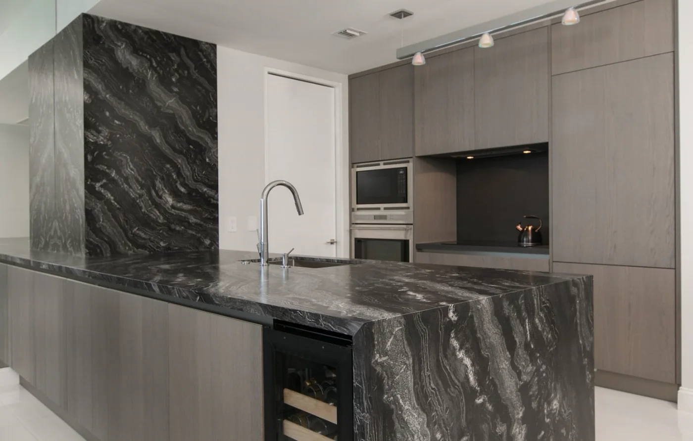 After: a black marble waterfall counter and grey cabinetry with built-in ovens