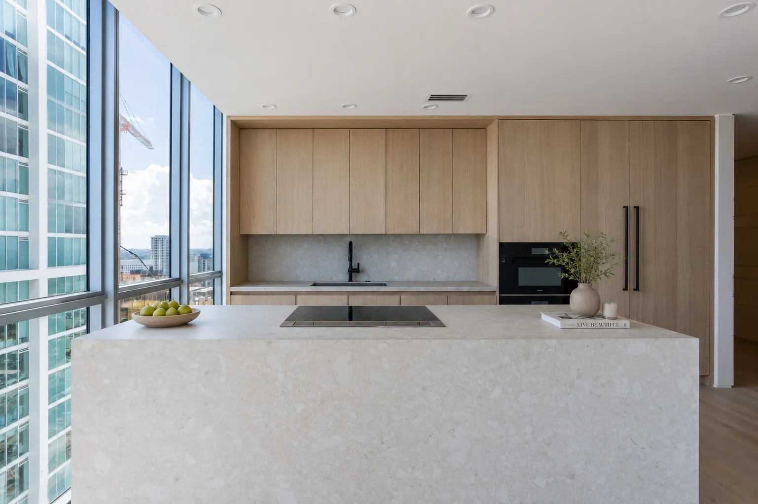 Marquis 3301 kitchen by DALOP Design: pale oak cabinetry and a stone waterfall island against floor-to-ceiling windows over the Miami bay