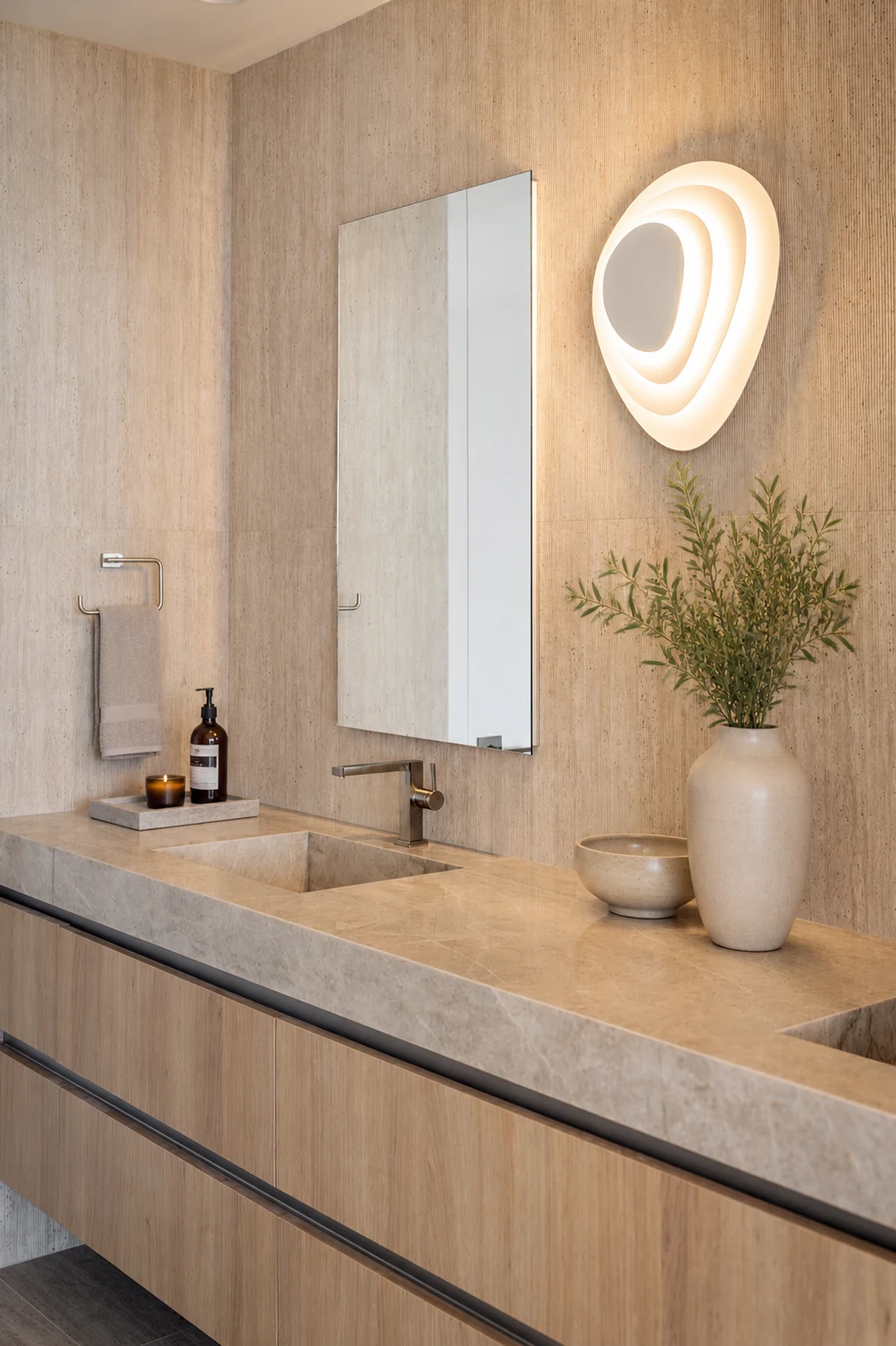 Marquis 3301 bathroom by DALOP Design: a floating oak vanity with a carved stone double basin and a sculpted wall light against travertine