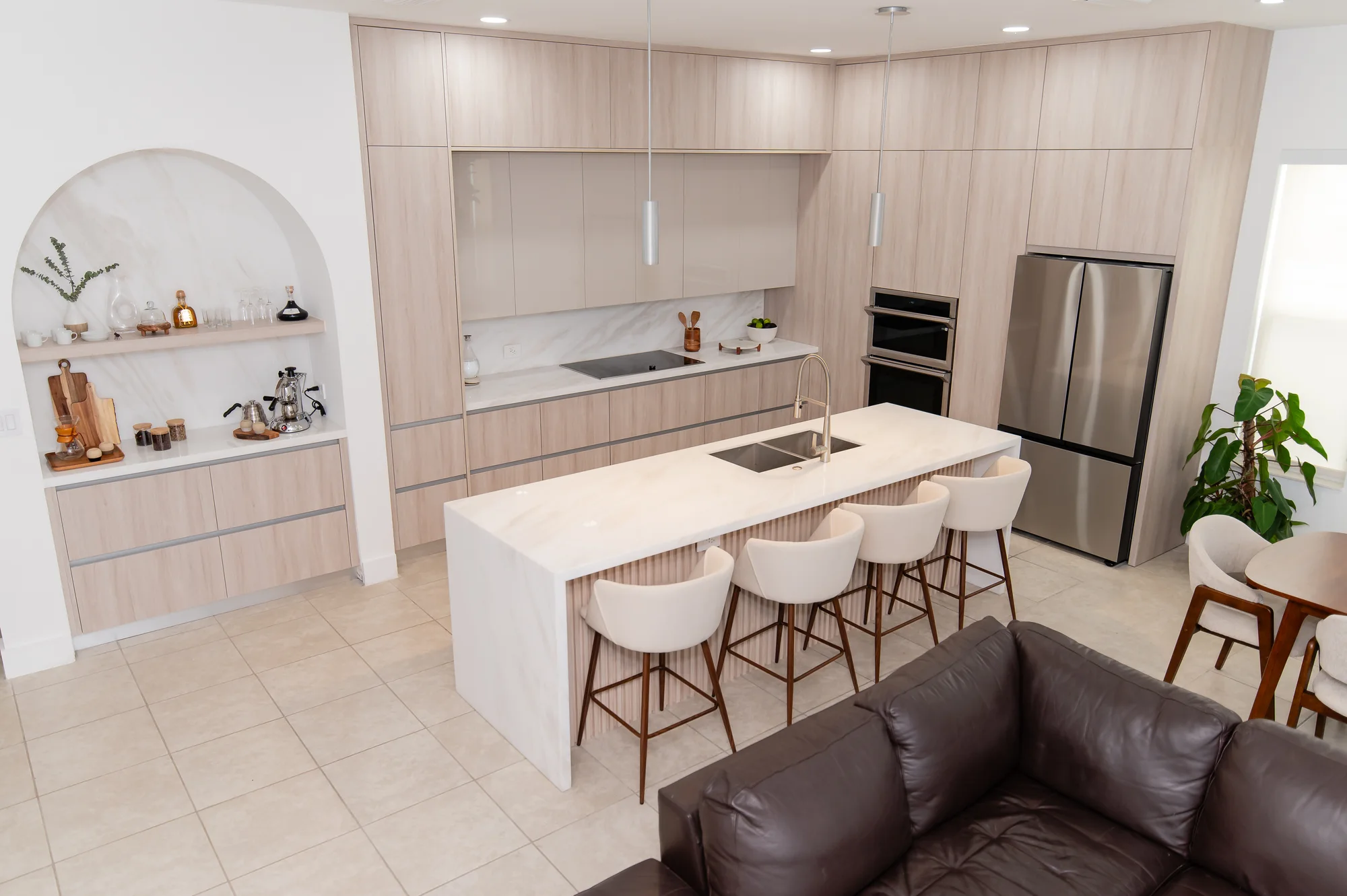 Open-plan pale oak kitchen with arched display shelves and a marble island seating five, designed by DALOP Design