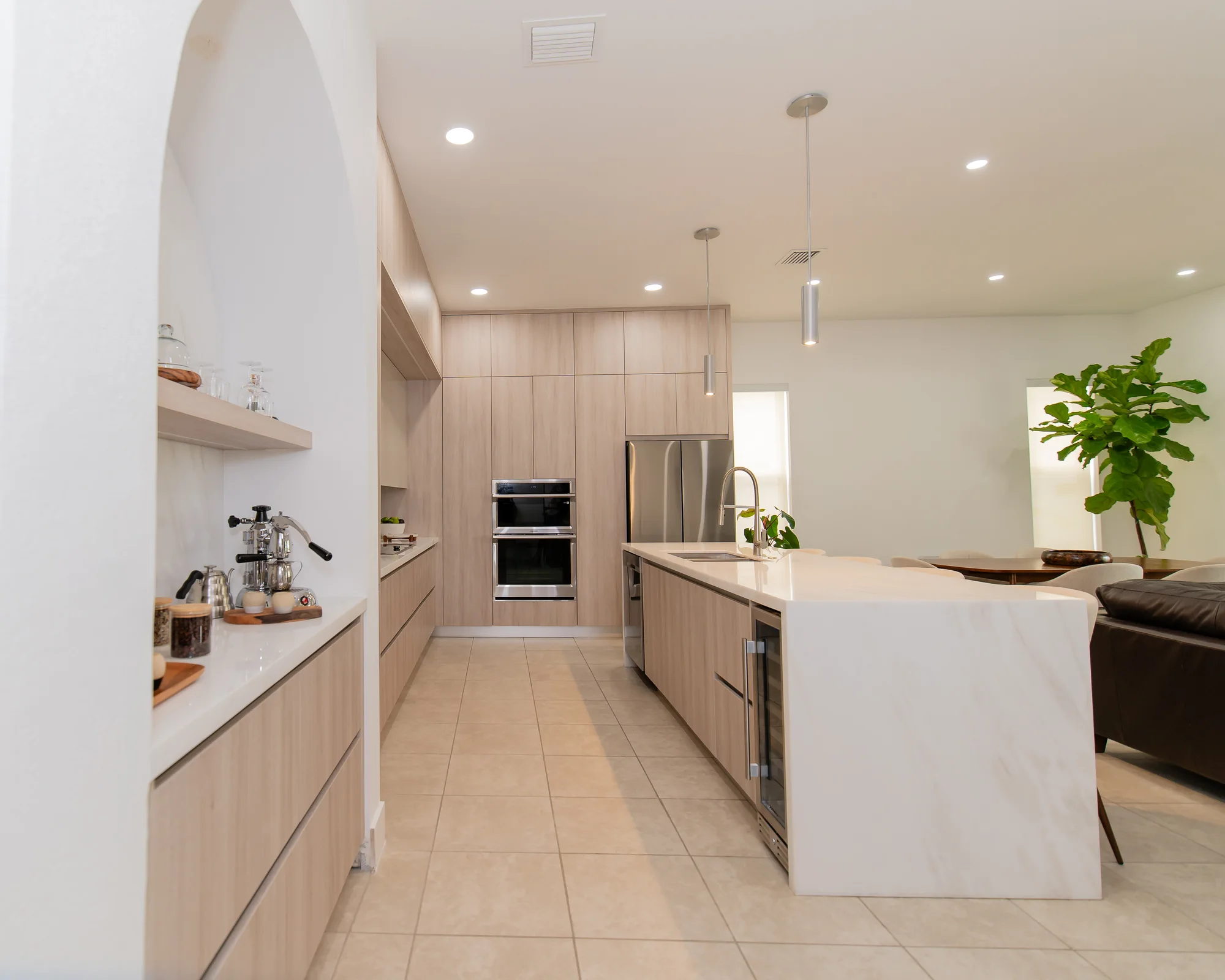 Pale oak kitchen with a marble waterfall island, open shelving and integrated ovens, designed by DALOP Design