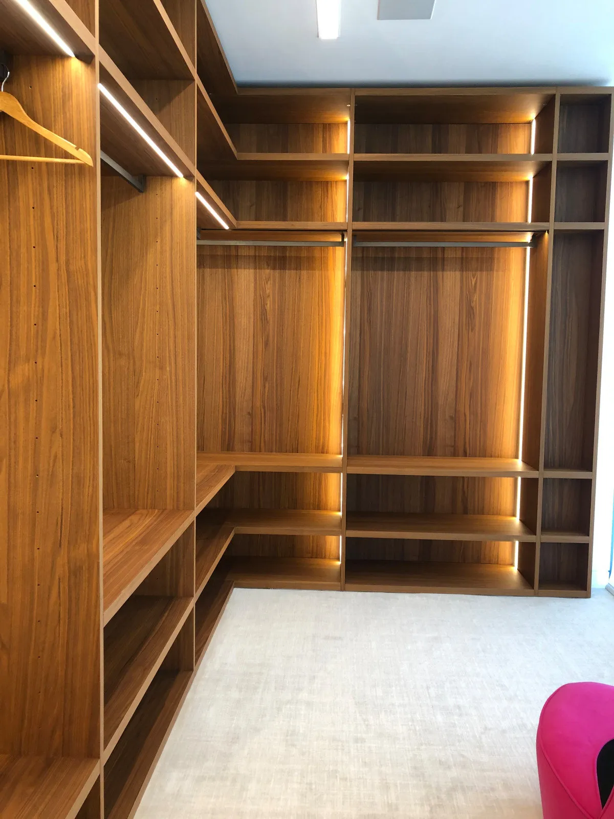 Walnut-toned walk-in closet with open shelving, hanging rails and drawer banks by DALOP Design