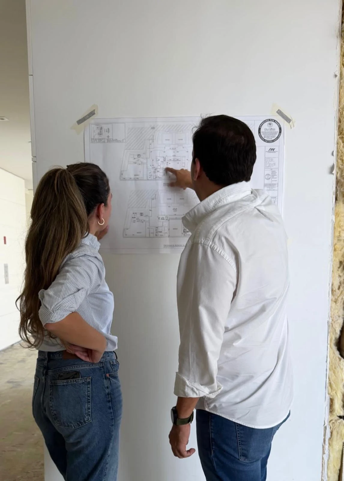 Daniela Lopez reviewing a floor plan pinned to the wall on a construction site with a builder